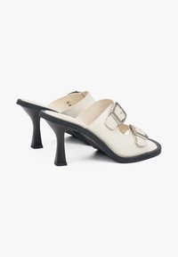 White leather mules with two adjustable straps and silver buckles. Black conical heel, square toe, smooth texture, and cut-out details.