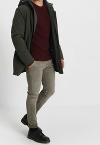 Grön isolerad parkas, texturerad bourgognesweater, ljusgrå skinnyjeans och svarta snörskor. Har fickor och huva.