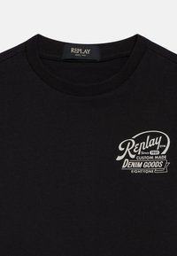 Camiseta de algodón negra con cuello redondo y mangas cortas, que presenta un logo blanco que dice "Replay Since 1981 Custom Made Denim Goods."