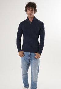 Pull-over tricoté navy avec un col haut et une fermeture éclair. Présente un motif de tricot torsadé. Assorti avec un jean bleu clair.