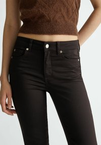 Bruine high-waisted jeans met een gladde textuur, metalen knoopaccenten en voorzakken. Strak slank ontwerp met een soepele afwerking.
