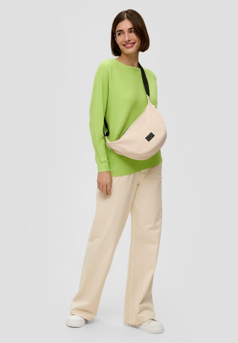 Helle rosa Umhängetasche mit glatter Textur, schwarzem Riemen und einem dezenten Etikett. Kombiniert mit einem leuchtend grünen gerippten Pullover und beigen Hosen.