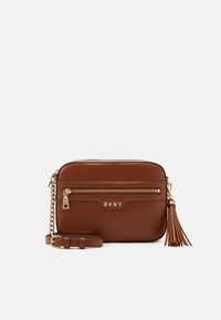 Brązowa torebka listonoszka DKNY wykonana z gładkiej skóry. Posiada złote okucia, przednią kieszeń na zamek oraz odpinany frędzel.