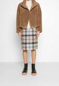 Bruine, pluizige nep bontjas met een kraag en twee knopen, gecombineerd met een beige geruite rok tot op de knie en zwarte enkellaarsjes met dikke zolen.