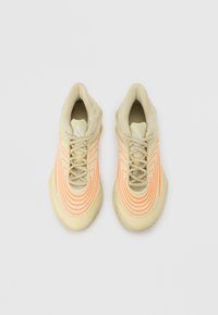 Beige athletic shoes with a stretchy upper, featuring wavy orange lines, a textured toe box, and standard laces. Rubber sole with pattern.