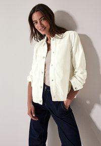 Witte button-up jas met een relaxed fit, voorzien van een platte kraag, zilveren drukknoopjes en opgerolde mouwen, gecombineerd met donkerblauwe broek.