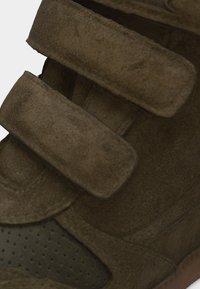 Κοντινό πλάνο καφέ σουέντ παπουτσιού με δύο φαρδιές λουρίδες βέλκρο και διακοσμητικές τρύπες κοντά στα δάχτυλα.