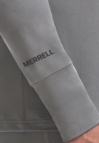 Gray athletic sweatshirt sleeve featuring a black "MERRELL" logo, smooth texture, structured cuff, and clean stitching detail.