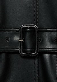 Gros plan d'une ceinture en cuir noir avec une boucle rectangulaire cousue et une broche métallique maintenant l'un des trous de la ceinture.