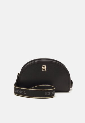 Czarna półokrągła torba na ramię z logo w kolorze złotym na przodzie oraz szerokim czarnym paskiem z beżowymi krawędziami i napisem "Tommy Hilfiger".