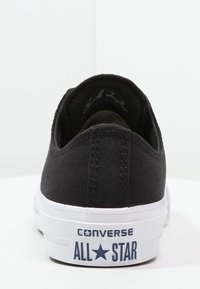 Černé plátěné tenisky s nízkým střihem, bílou gumovou podrážkou a označením "CONVERSE ALL STAR" na patě. Má minimální šití.