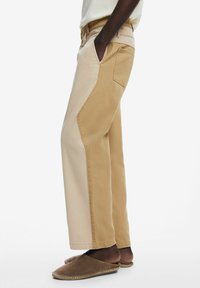 Beige and tan wide-leg trousers with contrasting side panels, made of cotton, featuring pockets and a relaxed fit. Textured fabric.