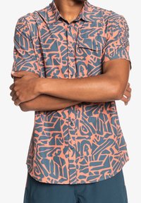 Koszula z krótkim rękawem o różowo-niebieskim abstrakcyjnym wzorze, wykonana z teksturowanej tkaniny, z kołnierzykiem i jedną kieszenią na piersi.