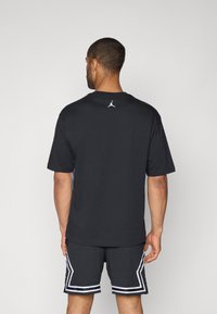 Camiseta de algodón negra con mangas cortas, que presenta un logo blanco de Jordan en la parte superior de la espalda, combinada con pantalones cortos de malla negros con acentos blancos.
