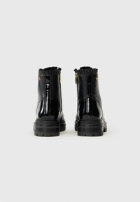 Botas de tobillo de charol negro con cuello texturizado con volantes, acentos de hardware dorado y suela gruesa negra. Detalle de cierre con cremallera lateral.