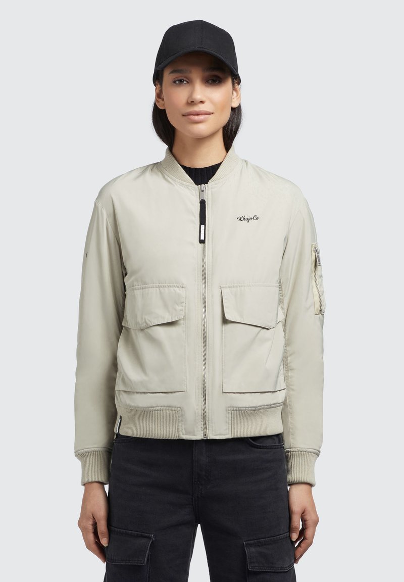 Heledahall hall musta bomber-jakk koos soonikkaelustega, kahe eesmise tasku ja tõmblukuga. Rinna peal on tikitud logo, millele on lisatud must peapael.