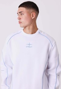 Witte sweatshirt met blauwe stiksels, ronde hals en geborduurd logo op de borst. Heeft een ontspannen pasvorm en een zachte textuur.