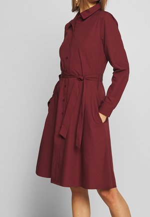 Vestido tipo camisa burdeos en tela de algodón, con cierre de botones al frente, mangas largas, cuello, cinturón en la cintura y bolsillos laterales.