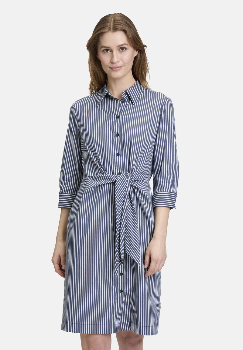 Abito a righe in blu navy e bianco, con una chiusura a bottoni, colletto, maniche a trequarti e un dettaglio in vita annodato. Tessuto dalla texture liscia.