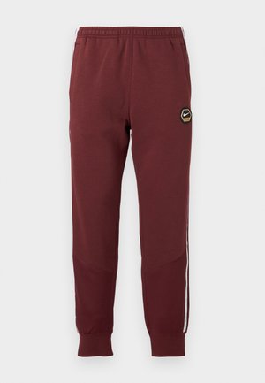 Chándal marrón con un logo hexagonal de Nike, cinturilla elástica, dos bolsillos laterales y rayas laterales blancas. Tejido texturizado con diseño de pierna ajustada.