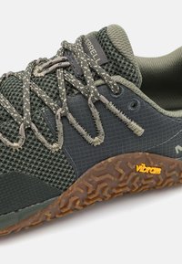 Tumši zaļi sieta un auduma sporta apavi ar teksturētām pelēkām akcentiem; aprīkoti ar pelēkām auklām, Vibram gumijas zoli un logotipa uzlīmi uz mēles.