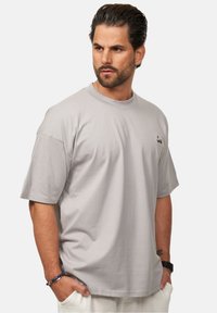 Graues Baumwoll-T-Shirt mit Rundhalsausschnitt und kurzen Ärmeln. Verfügt über ein kleines gesticktes Design auf der Brust. Sanfte Textur, lockere Passform.