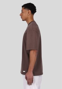 Brown cotton T-shirt with a crew neckline, short sleeves, and a straight cut. Features a small white label at the hem.