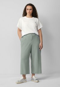 Lichtgroene wijde broek met zijzakken, gecombineerd met een witte t-shirt met korte mouwen en een klein, multicolored geborduurd ontwerp. Zilveren sneakers.
