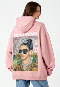 Felpa oversize rosa con stampa grafica di una donna con occhiali da sole, con la didascalia "ART IS EXPENSIVE", valorizzata da un orlo a costine.