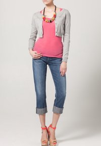 Grå cardigan över en rosa top, matchad med uppvikta blå jeans och beige kilklackar med korallfärgade ankelremmar. Färgglad pärlsmycke.