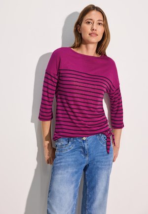 Haut rayé fuchsia et violet profond avec des manches trois-quarts, noué à la taille, associé à un jean large bleu clair.