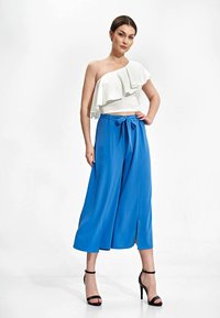 Witte schouderloze top met ruches, gecombineerd met losse, felblauwe culottes met een strik op de taille en uitsparingen.