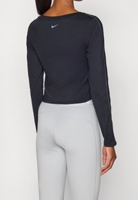 Schwarzes langärmliges Sportoberteil mit rundem Halsausschnitt. Mit blauem Nike-Logo auf dem Rücken und grauen Sportleggings. Glatte Textur.
