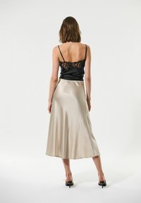 Un caraco noir en satin avec des détails en dentelle, associé à une jupe en soie fluide et longueur cheville de couleur beige clair, présentant une texture lisse et un léger éclat.