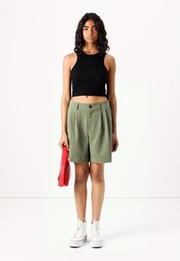 Crop top noir à côtes, shorts plissés vert olive, sac à main rouge et baskets montantes blanches. Design simple avec des couleurs et des textures contrastées.