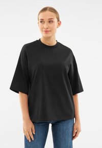Tricou oversize negru din bumbac moale, cu guler pătrat și mâneci scurte. Purtați-l cu blugi denimi albaștri.