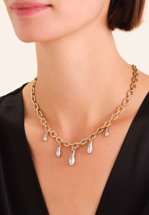 Collana a catena d'oro con cinque pendenti a goccia d'argento, caratterizzata da grandi maglie e una finitura lucida, indossata su una maglia scura.
