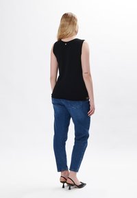 Top nero senza maniche, tessuto liscio, scollatura rotonda, dettaglio dorato sul retro; abbinato a jeans blu, vestibilità a taper, tasche posteriori, orli risvoltati.