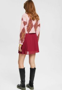 Textureret lyserød og burgunder argyle sweater, parret med en plisseret burgunder nederdel og knæhøje sorte støvler med kraftige såler.