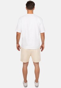 Witte korte mouwen t-shirt met een ronde hals, gecombineerd met beige shorts en witte sneakers, gezien vanaf de achterkant, eenvoudig ontwerp.