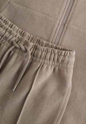 Joggers beiges en tissu texturé, dotés d'une taille élastique avec cordon de serrage et de poches latérales, présentant une finition lisse.