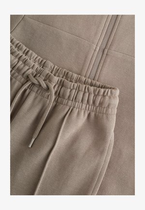 Béžové tepláky vyrobené z texturovanej látky, s elastickým pásom a šnúrkou, bočnými vreckami a hladkým povrchom.