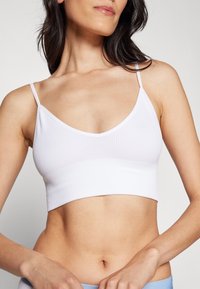 Hvit ribbet bralette med tynne justerbare stropper. Har en V-hals og en cropped passform, som viser en glatt tekstur og minimalistisk design.