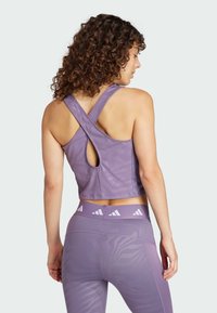 Lilla atletisk crop top med krydsryg-design, der har en nøglehulåbning på ryggen. Materialet virker glat med en let glans.