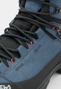 La botte de randonnée en suède bleu présente des accents synthétiques noirs, des boucles de lacet texturées et des détails orange sur les lacets pour une meilleure visibilité.