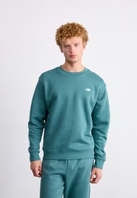 Teal katoenen sweatshirt met een ronde hals en geribde manchetten, met een klein wit logo op de linkerkant van de borst. Glad textuur, losse pasvorm.