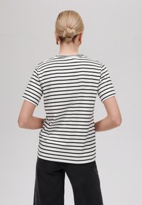 Kortermet t-skjorte i hvitt med svarte horisontale striper. Klassisk rund halsdesign, laget av mykt stoff med en glatt tekstur.