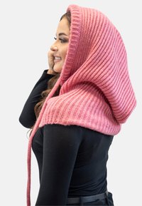 Wrap con cappuccio lavorato a maglia di colore rosa con texture a coste e lunghe fasce, caratterizzata da un design accogliente che drappeggia sulle spalle e sulla schiena.