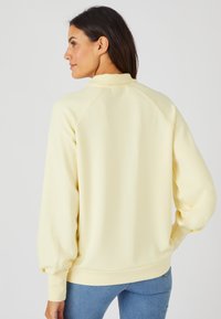 Sudadera de color amarillo claro con cuello redondo, mangas raglán y puños de canalé. Tejido suave con un ajuste relajado y detalles mínimos.