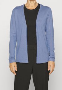Cardigan bleu clair à manches longues, design à devant ouvert, texture douce et poignets côtelés, associé à un haut noir et un pantalon noir.